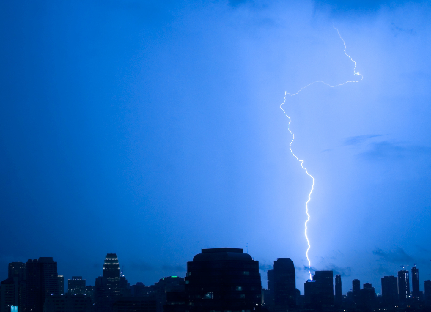 春の夕空の下、街並みの向こうに一本の稲妻が落ちる雷の風景