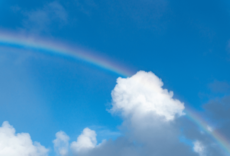 青空に白い雲と淡い虹が弧を描く風景