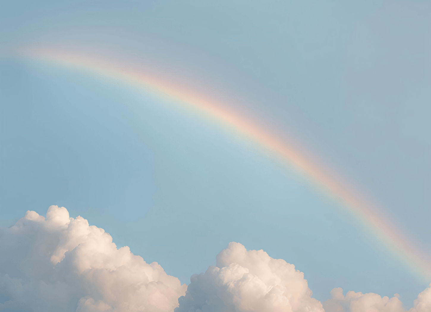 やわらかな青空に淡い虹が斜めにのびる景色